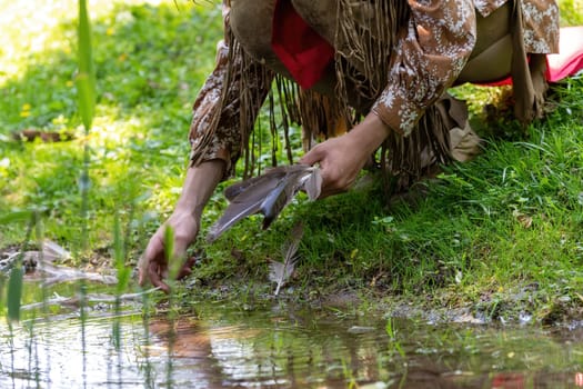 Man in Indian clothing picks up a bird's feather in a meadow on the banks of a stream