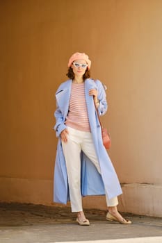Stylish woman in long trench, breeches and hat standing in arch