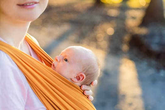 A loving mother walks through a peaceful park, carrying her baby securely in a sling. A heartwarming moment of maternal bonding, babywearing, and the joy of motherhood in nature.