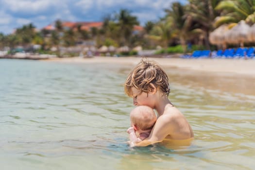 An older brother gently holds his baby sibling while swimming in the sea, sharing a joyful and heartwarming moment of family bonding and summer fun in the water. A perfect blend of love, care, and childhood adventure.