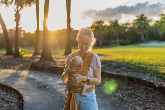A loving mother walks through a peaceful park, carrying her baby securely in a sling. A heartwarming moment of maternal bonding, babywearing, and the joy of motherhood in nature.