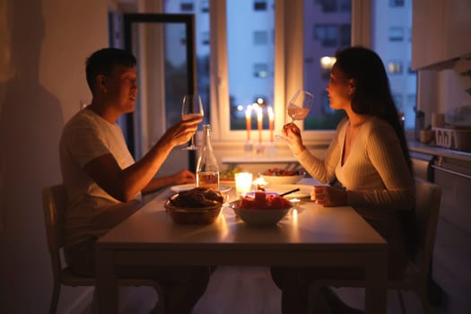 Young couple toasting with wine glasses during romantic candlelit dinner at home