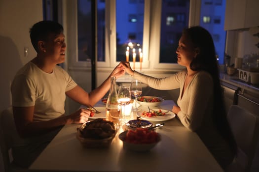 Happy couple enjoying romantic evening with candles and wine, celebrating their love