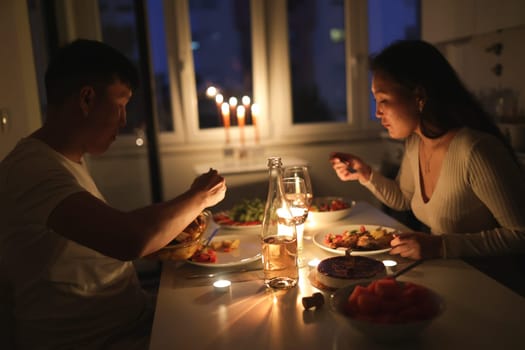 Young couple having a romantic candlelit dinner at home, enjoying delicious food and wine