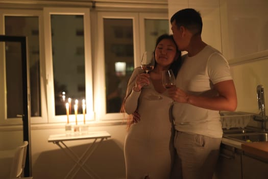 Couple embracing and drinking wine in a candlelit kitchen, creating a romantic and intimate atmosphere