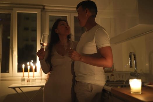 Asian couple enjoying a romantic evening, drinking wine by candlelight in their kitchen