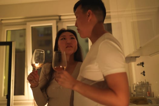 Asian couple drinking wine and talking in a kitchen at night