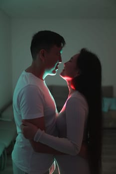 Asian couple embracing tenderly in a dimly lit room, illuminated by colorful neon lights, creating a romantic atmosphere
