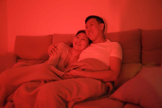 Asian couple enjoying a relaxing evening together, cuddling on the sofa under a warm red light