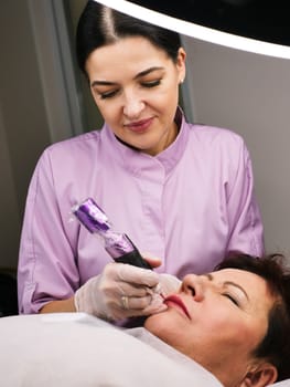 Permanent makeup artist tattoos a beautiful woman over 50 years old in a beauty salon on the client's face. Vertical