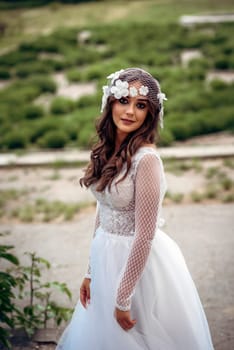 young girl bride in a white dress in a spring forest on a wedding day, beautiful brunette in a long stylish plan among huge trees. hair veil with flowers in vintage style