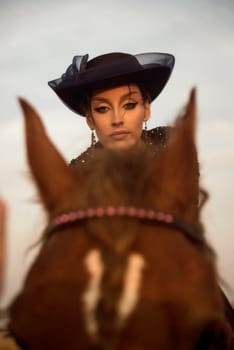 portrait of beautiful equestrian woman who is engaged in horse riding. charming girl in long blue dress. elegant style with gloves and hat. rider is walking in the field. concept of women riding horses
