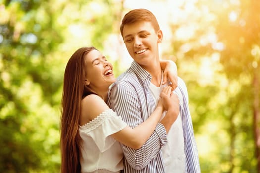 Pretty young girl laughing and hugging her handsome boyfriend at summer park
