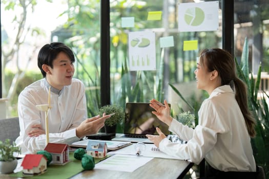 Professionals engage in strategies for eco-residential development, discussing models and visuals while harnessing innovative ideas in a green workspace.