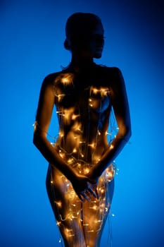A woman stands gracefully, adorned with glowing lights, creating a captivating silhouette against a blue backdrop.