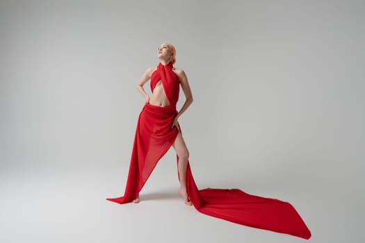 A woman stands confidently, adorned in flowing red fabric that accentuates her beauty and grace in a well-lit studio setting.
