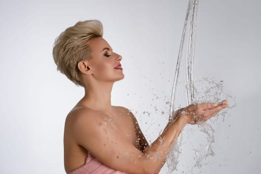 A beautiful woman is playfully interacting with water, showcasing her elegance and confidence in a serene setting.