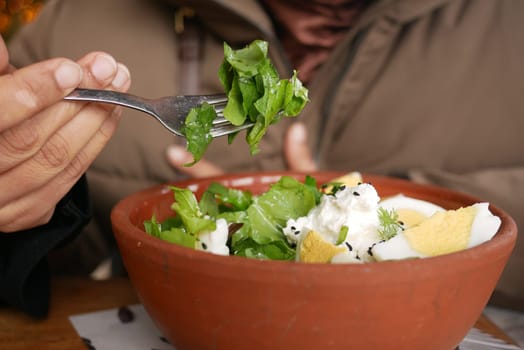 A person is eating a vibrant salad with greens and toppings at a table.