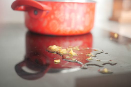Oil is spilled on a countertop beside a red pot after cooking.