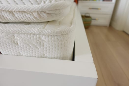 Soft white mattresses stacked on a sleek white bed frame in a cozy room.