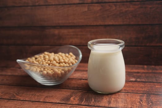 Fresh soy milk sits next to a bowl of raw soybeans on wood.