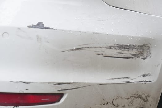 Bumper of a white car showing scratches and damage from an accident.