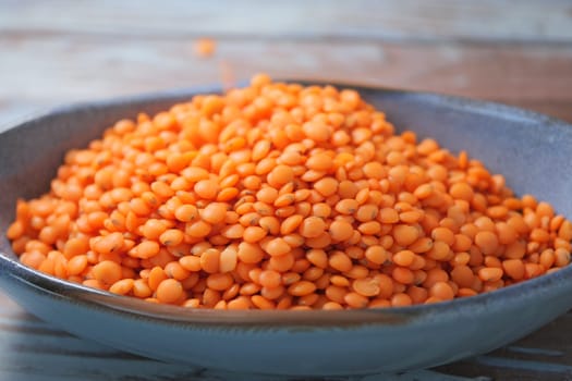 A mound of vibrant orange lentils fills a shallow bowl on a rustic table.