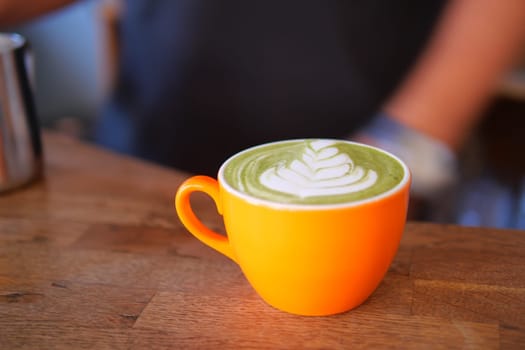 Delicious matcha latte served in vibrant orange cup on wooden table,