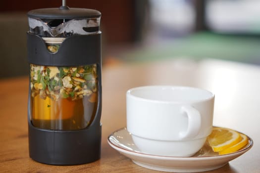 A cylindrical tea infuser sits next to a steaming cup of herbal tea.
