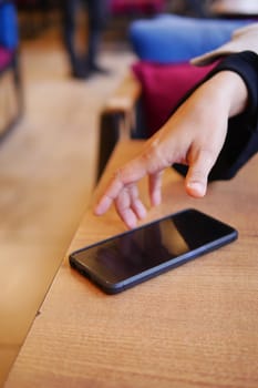 A person extends their hand toward a smartphone resting on a table.
