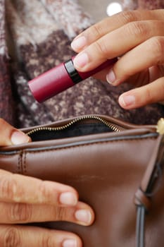 A person retrieves a lipstick from their brown purse in nature.