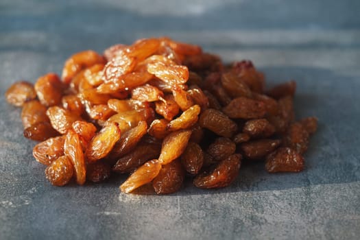 A pile of golden raisins rests on a textured surface with bright lighting.