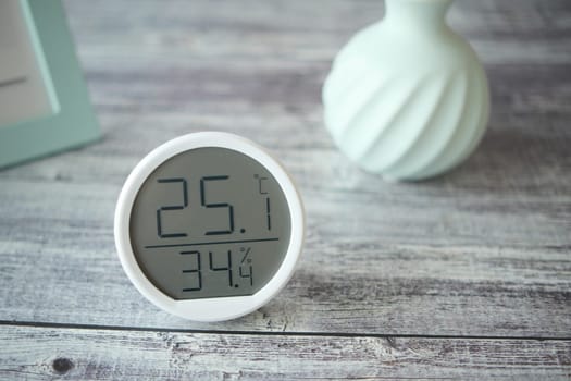 Digital device displays temperature and humidity beside a vase.