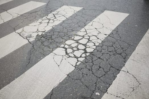 A worn crosswalk shows extensive cracks and wear from heavy traffic.