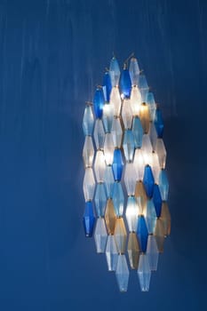 Colorful hexagonal light fixture illuminates a deep blue wall.