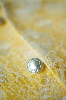 Silver button shines on textured yellow fabric, creating a captivating contrast.
