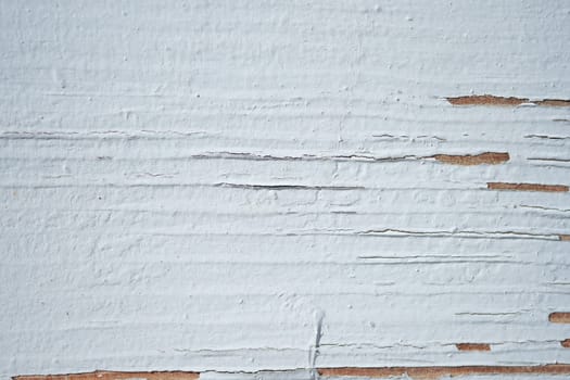 A close-up view of a weathered wall showing peeling white paint.