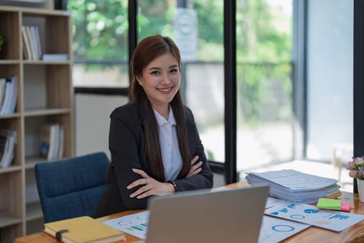 Confident business woman smiling Show successful gestures at her desk with market charts and documents in office.