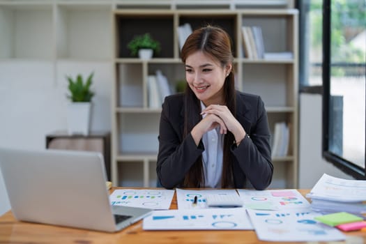 Confident business woman smiling Show successful gestures at her desk with market charts and documents in office.