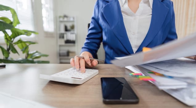A focused professional woman in a blue blazer is engaged in tax calculations, surrounded by financial documents and a calculator, highlighting her dedication to business and finance.