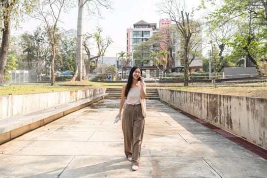 A woman enjoys her walk in an urban park, confidently holding her reusable cup and bag, embodying a sustainable lifestyle and positivity.