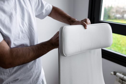 Adult caucasian male adjusting modern white office chair near window on sunny day.