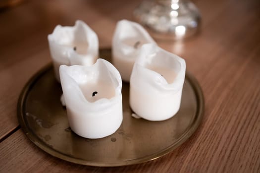 Melted white candles on brass tray with wooden surface background.