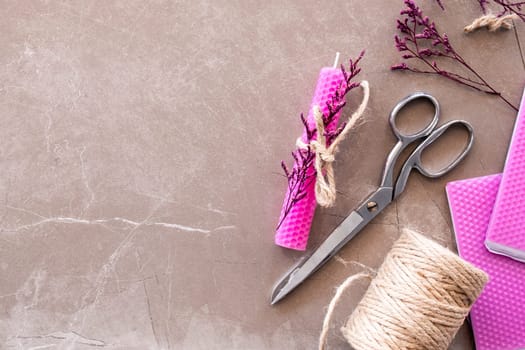 Creative candle crafting with beeswax, scissors, and twine on marble surface.