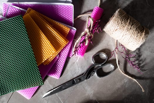 Colorful wax sheets with scissors twine and wrapped candle on a stone surface.
