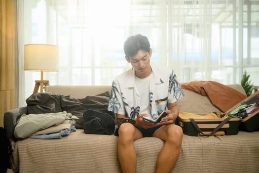 Young traveler preparing for an upcoming journey, sitting on sofa and organizing his belongings.