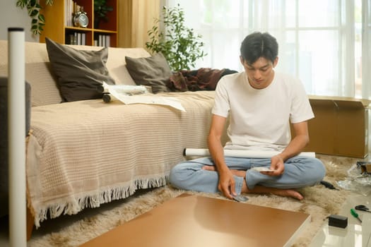Focused asian man assembling a piece of furniture. Home organization and interior decorating concept.