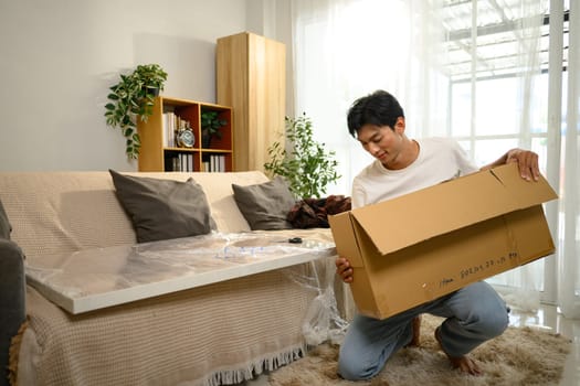 Smiling young man unpacking and assembling a piece of furniture in a living room.