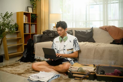 Man using digital tablet to checking maps or confirming accommodations while packing for summer vacation.