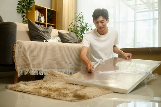 Smiling young man unpacking and assembling a piece of furniture in a living room.